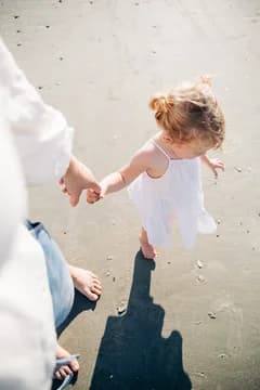 Mom Holding Hand of Young Daughter Walking on Beach
