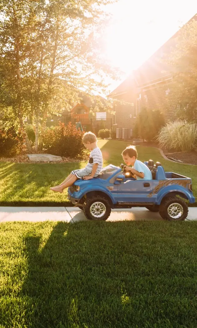 Two boys playing with toy car on sidewalk by the house