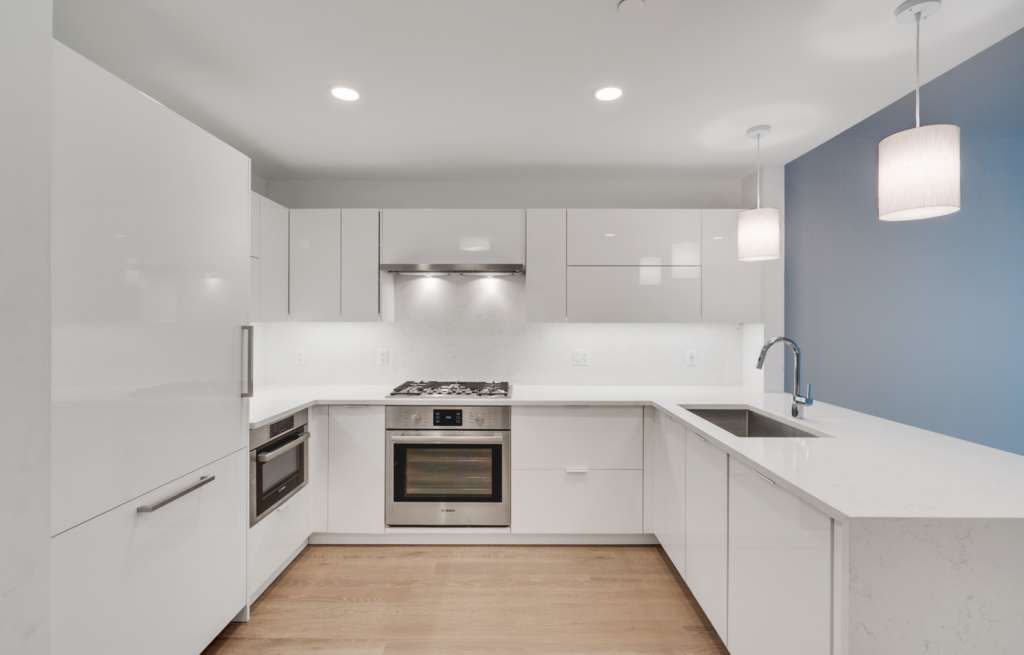 White U-shaped kitchen with refrigerator on the left, oven in the middle and sink on the right.